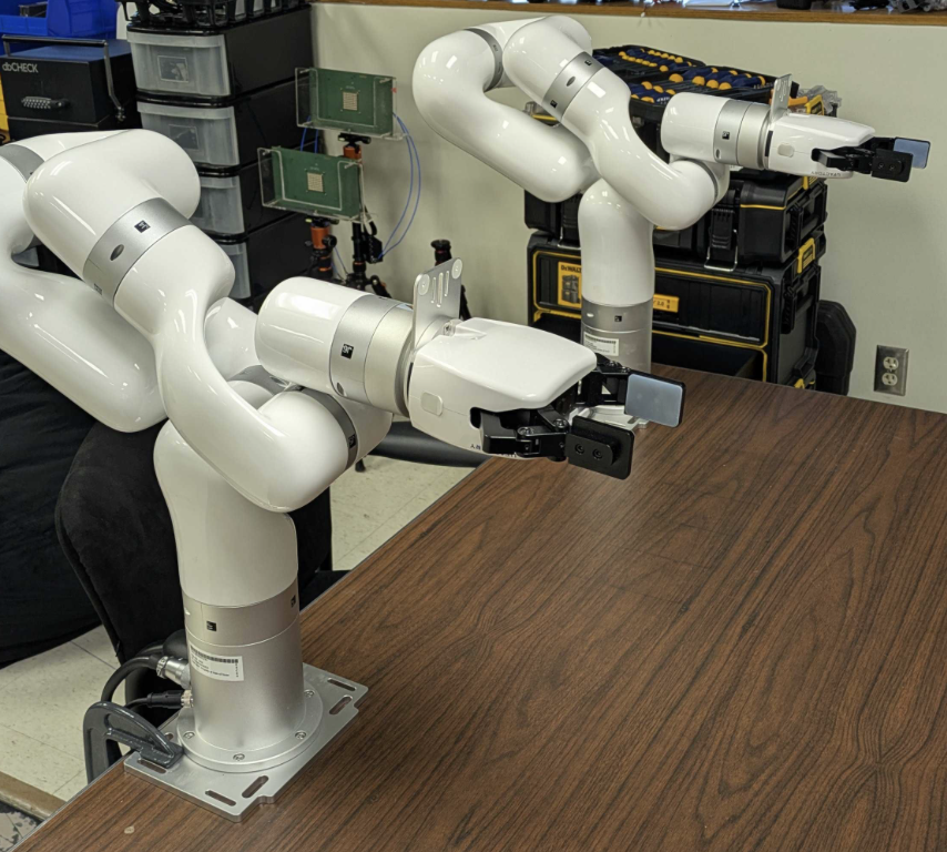 Two robotic arms mounted near a lab table for leader/follower robotics experiments.