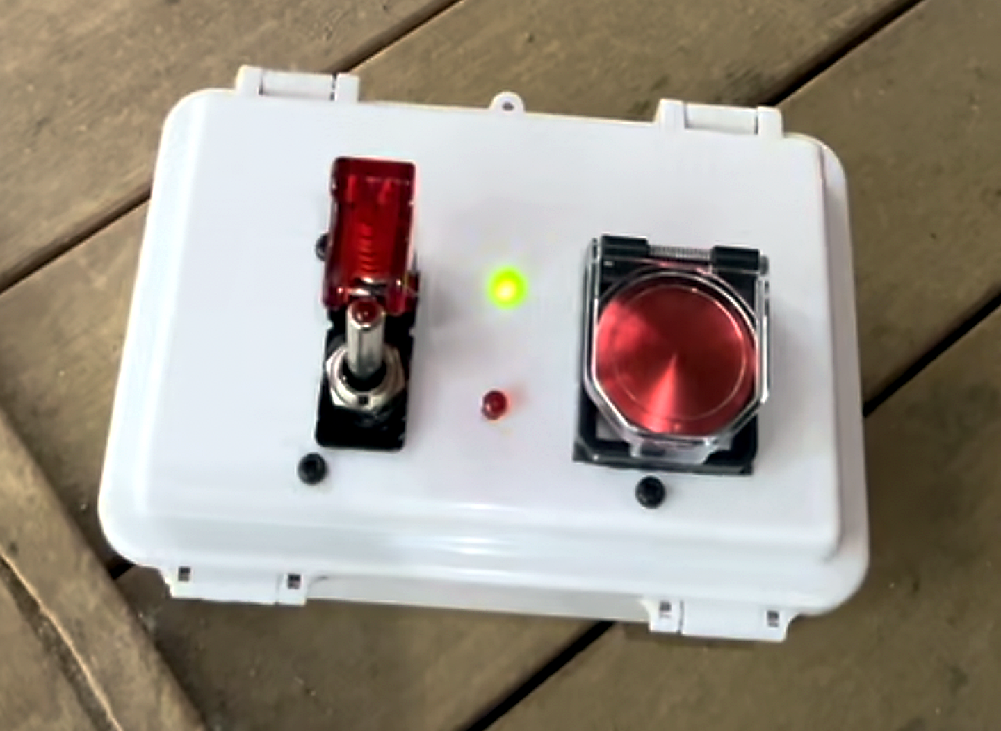 White remote-control box with a red safety switch, indicator lights, and a large red button.